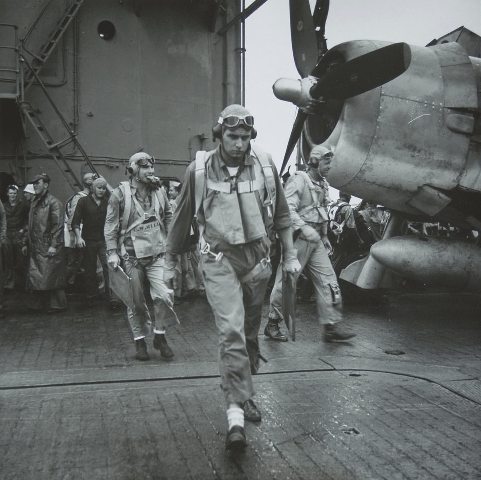 A WW 2 Steichen image of Pilots walking along the flight deck, with what appears to be a Vought F4U Corsair in the background.